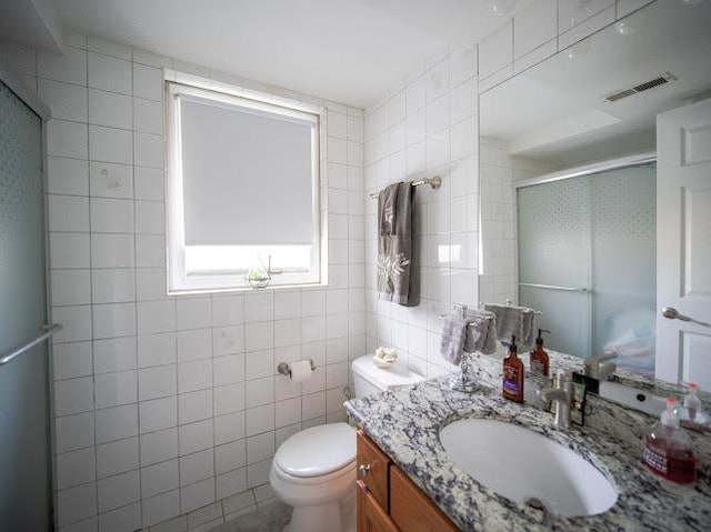 bathroom with visible vents, vanity, a shower stall, and tile walls