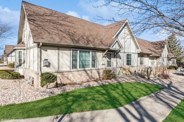 tudor house with roof with shingles, brick siding, a front lawn, and stucco siding