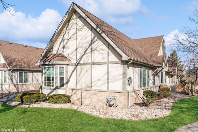 view of side of home featuring a yard, a shingled roof, brick siding, and stucco siding