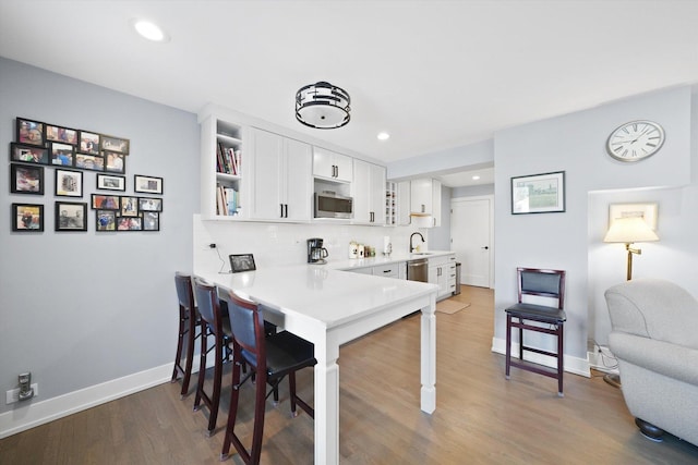 kitchen featuring appliances with stainless steel finishes, a breakfast bar area, wood finished floors, white cabinetry, and open shelves