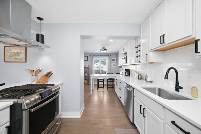 kitchen featuring stainless steel appliances, a sink, white cabinetry, decorative backsplash, and wall chimney exhaust hood