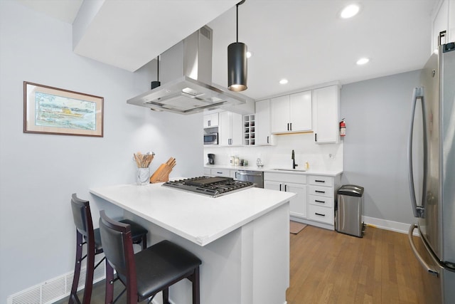 kitchen featuring a kitchen bar, appliances with stainless steel finishes, a sink, a peninsula, and wall chimney exhaust hood