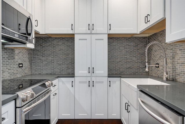 kitchen featuring a sink, backsplash, dark countertops, stainless steel appliances, and white cabinets