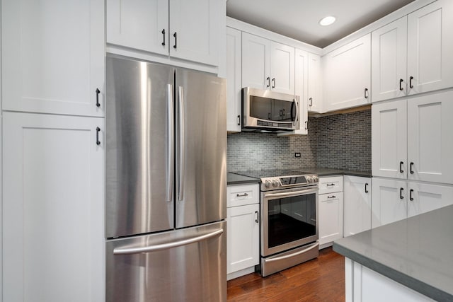 kitchen with stainless steel appliances, decorative backsplash, dark wood-type flooring, white cabinetry, and dark countertops