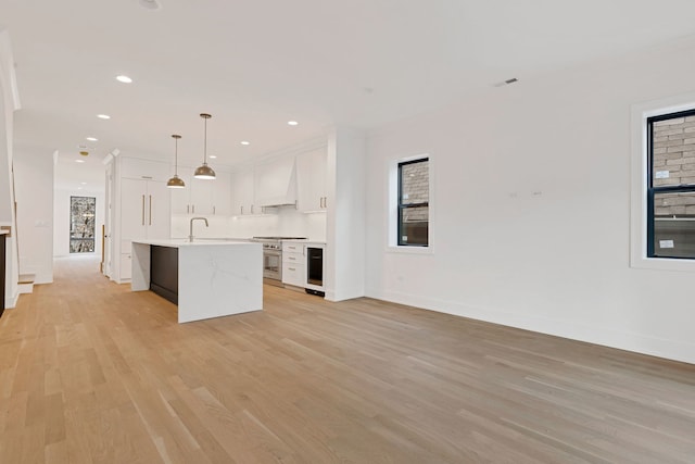 kitchen with decorative light fixtures, a center island with sink, light countertops, white cabinets, and premium range hood