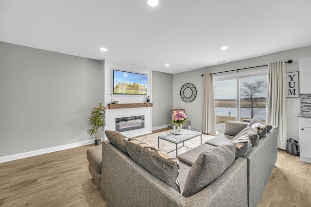 living room featuring a large fireplace, baseboards, wood finished floors, and recessed lighting