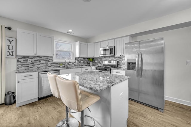 kitchen featuring a kitchen island, appliances with stainless steel finishes, a kitchen bar, white cabinetry, and a sink