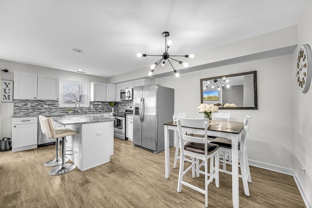 kitchen with a center island, backsplash, appliances with stainless steel finishes, white cabinets, and light stone countertops