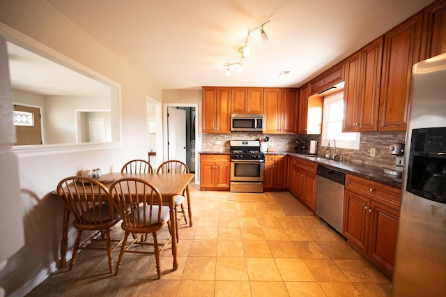 kitchen with light tile patterned floors, a sink, appliances with stainless steel finishes, tasteful backsplash, and brown cabinetry