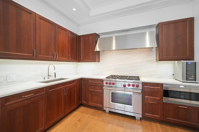 kitchen featuring stainless steel appliances, light countertops, decorative backsplash, a sink, and wall chimney range hood