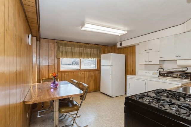 kitchen with range with gas stovetop, light countertops, freestanding refrigerator, white cabinets, and wood walls