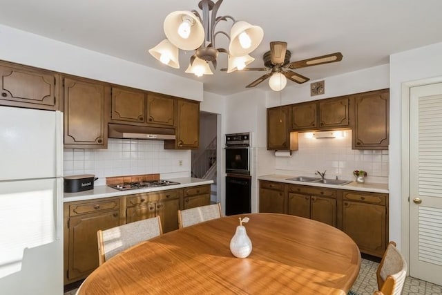 kitchen with under cabinet range hood, a sink, light countertops, freestanding refrigerator, and stainless steel gas stovetop