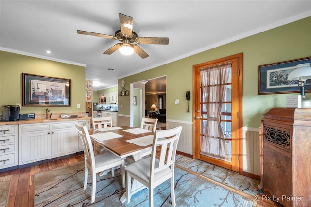 dining area with ceiling fan, ornamental molding, wainscoting, and wood finished floors