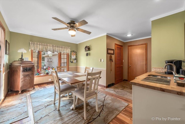 dining space featuring a wainscoted wall, crown molding, a ceiling fan, and light wood-style floors