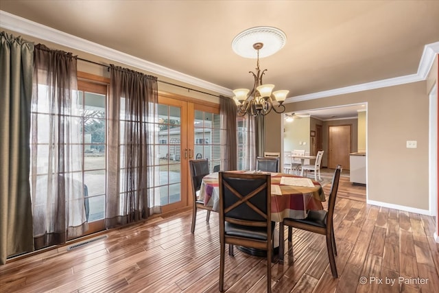 dining room featuring wood finished floors, visible vents, baseboards, ornamental molding, and an inviting chandelier