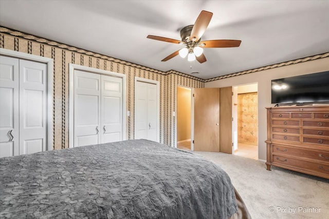 bedroom with carpet, two closets, a ceiling fan, ensuite bath, and wallpapered walls