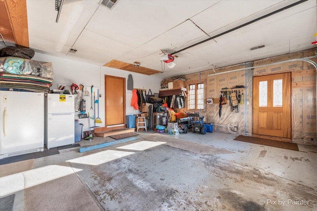 garage featuring a garage door opener, freestanding refrigerator, and visible vents