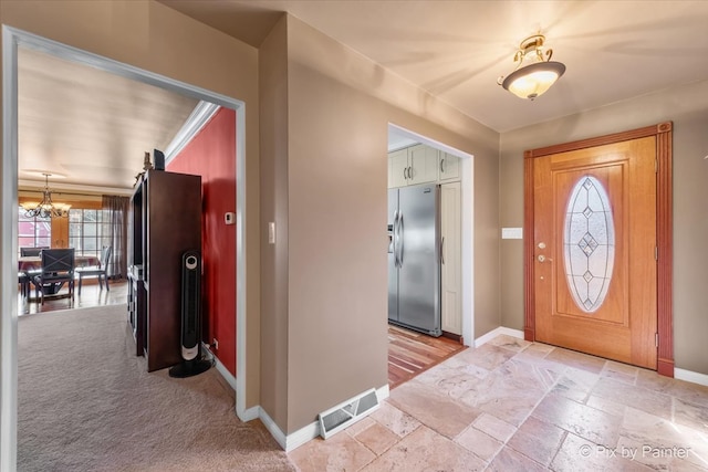 entryway featuring a notable chandelier, light carpet, stone tile floors, visible vents, and baseboards