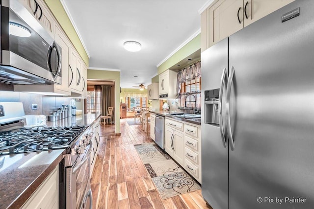 kitchen with crown molding, light wood-style flooring, decorative backsplash, appliances with stainless steel finishes, and a sink