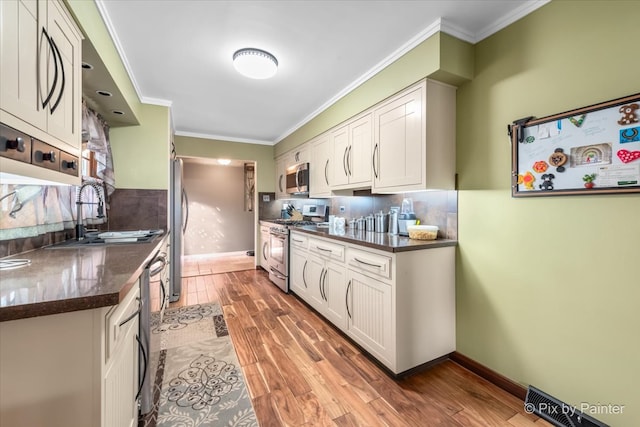 kitchen featuring stainless steel appliances, dark countertops, light wood-type flooring, and ornamental molding