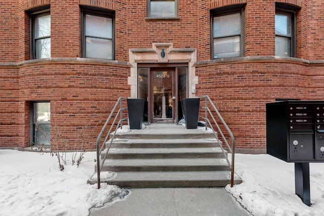 snow covered property entrance featuring brick siding