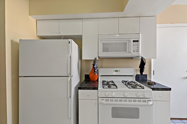 kitchen featuring dark countertops, white appliances, and white cabinets