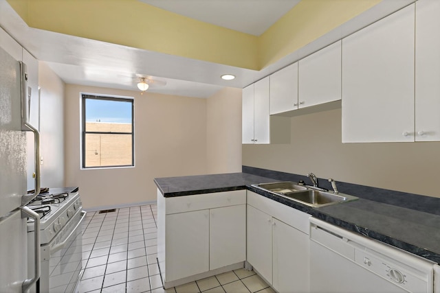 kitchen with dark countertops, white cabinets, a sink, white appliances, and a peninsula