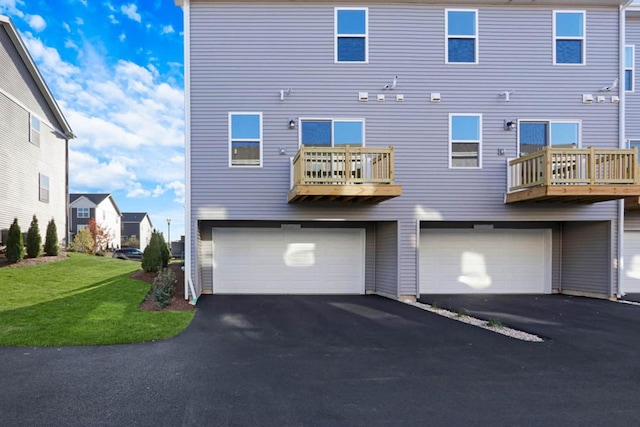 back of house featuring a garage, a lawn, driveway, and a balcony