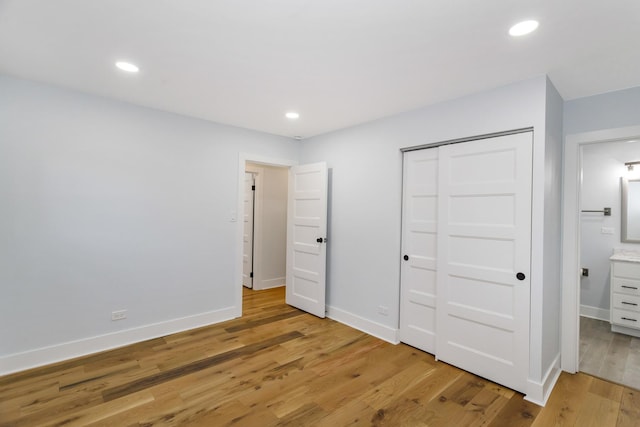 unfurnished bedroom with recessed lighting, baseboards, light wood-style floors, a closet, and ensuite bath