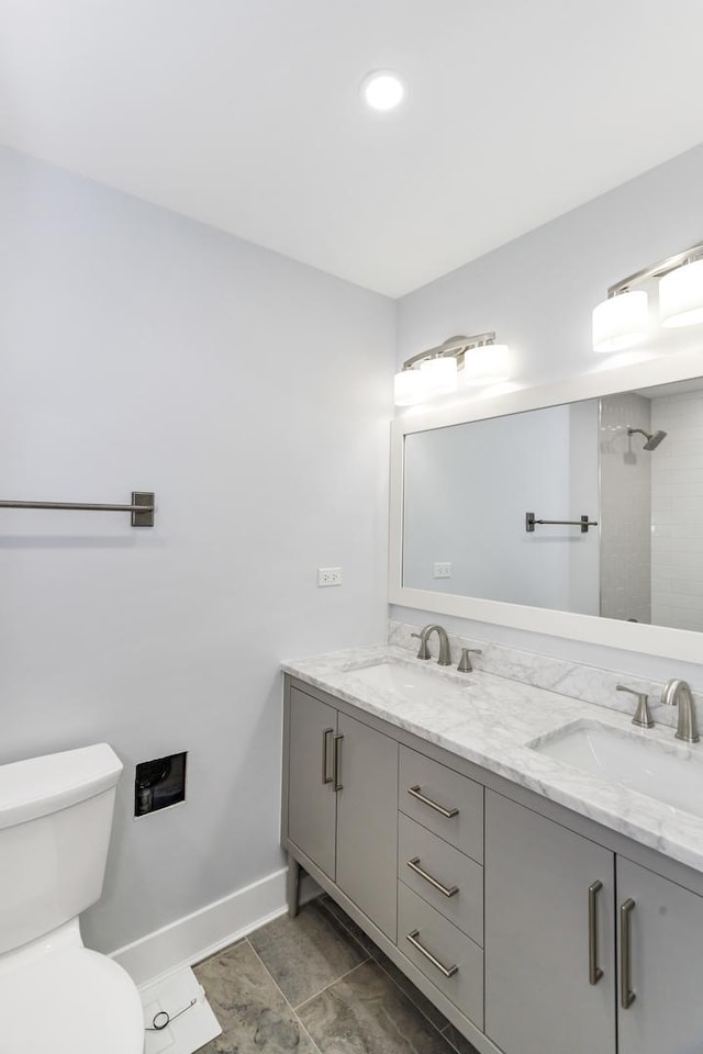 full bathroom with double vanity, a sink, toilet, and baseboards