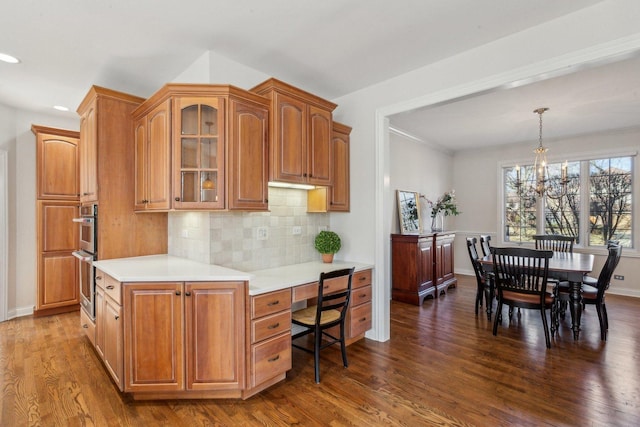 kitchen featuring dark wood-style floors, decorative light fixtures, tasteful backsplash, light countertops, and glass insert cabinets