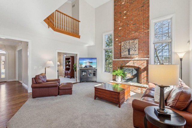 carpeted living room with a fireplace, wood finished floors, a towering ceiling, and baseboards