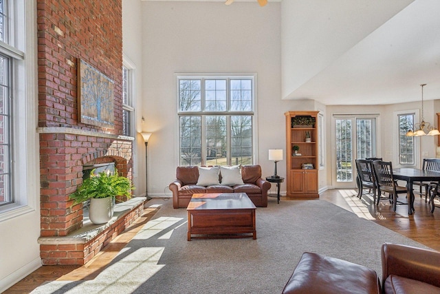 living area featuring a towering ceiling, a fireplace, baseboards, and wood finished floors