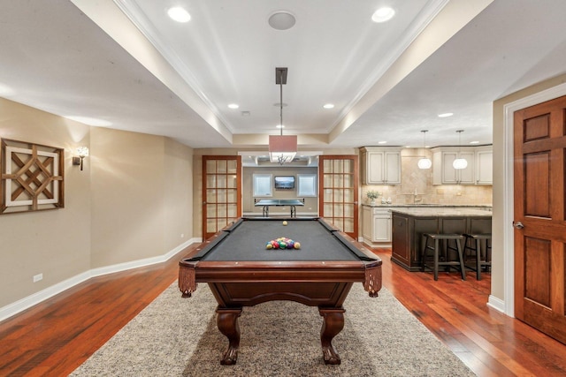 game room with ornamental molding, dark wood-style flooring, a raised ceiling, and baseboards