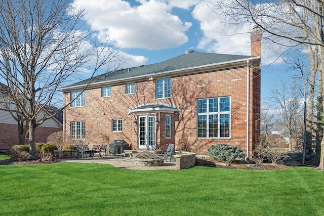 rear view of house featuring a patio area, a yard, a chimney, and brick siding