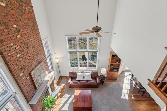 living room with a ceiling fan, a towering ceiling, baseboards, and wood finished floors