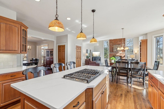 kitchen with stainless steel gas cooktop, backsplash, an inviting chandelier, light wood-style floors, and glass insert cabinets