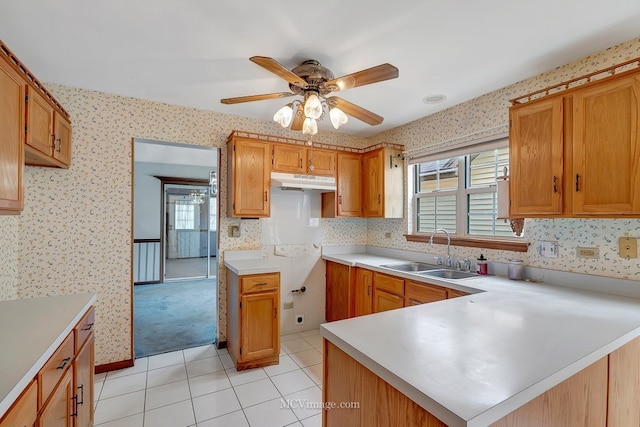 kitchen featuring light countertops, a sink, a peninsula, under cabinet range hood, and wallpapered walls