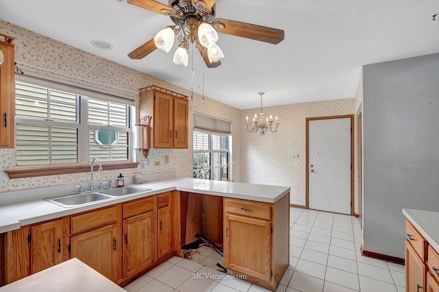 kitchen with light tile patterned floors, a peninsula, a sink, light countertops, and wallpapered walls