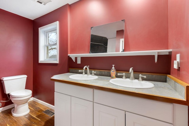 bathroom with double vanity, a sink, toilet, and wood finished floors