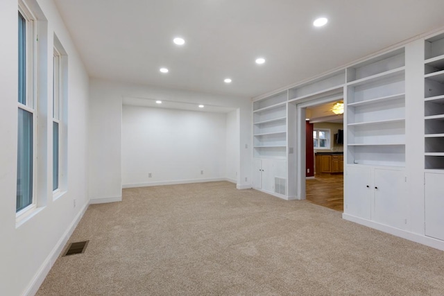 empty room with built in shelves, recessed lighting, light colored carpet, visible vents, and baseboards