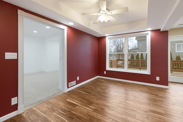 unfurnished room with a raised ceiling, recessed lighting, wood finished floors, and baseboards