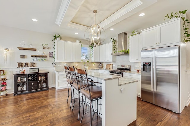 kitchen with stainless steel appliances, dark wood-type flooring, backsplash, wall chimney exhaust hood, and a tray ceiling