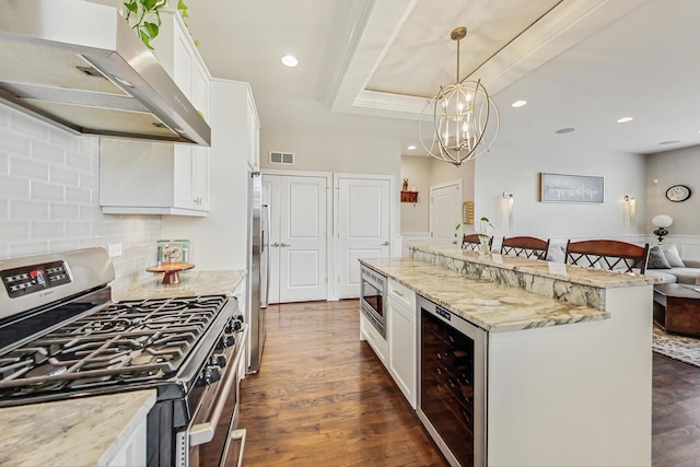 kitchen with tasteful backsplash, visible vents, wall chimney exhaust hood, wine cooler, and stainless steel appliances