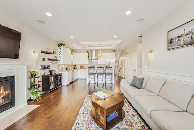 living area featuring recessed lighting, a wainscoted wall, dark wood-type flooring, a glass covered fireplace, and a raised ceiling