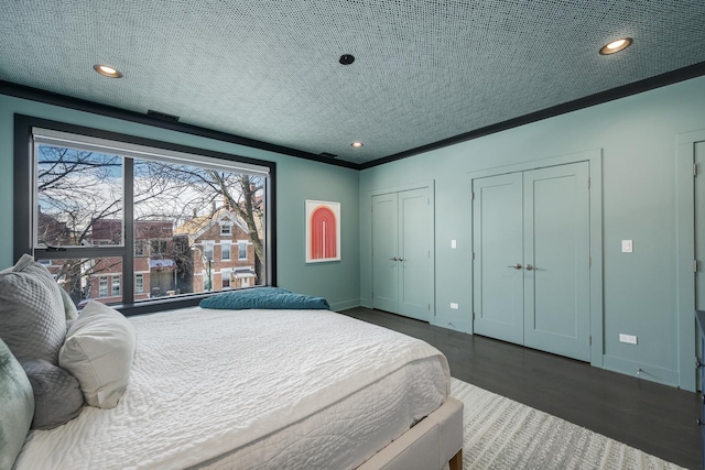 bedroom with a textured ceiling, ornamental molding, two closets, and baseboards