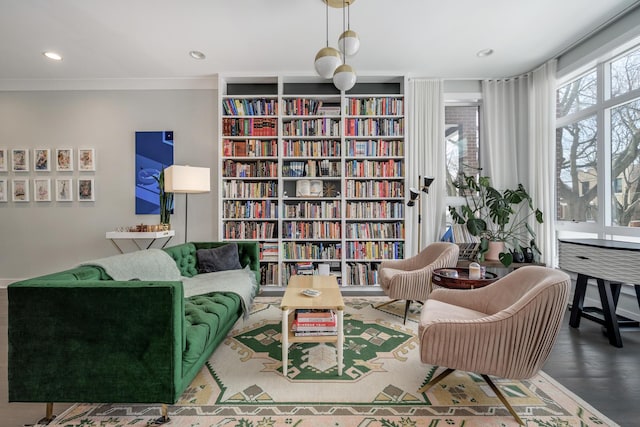 living area featuring wall of books, ornamental molding, wood finished floors, and recessed lighting