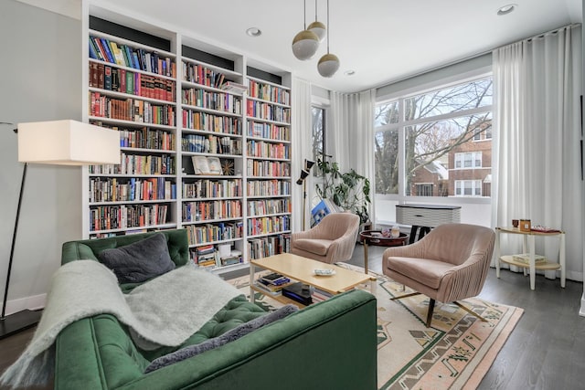 living area with recessed lighting, bookshelves, baseboards, and wood finished floors