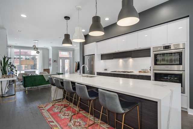 kitchen with a center island with sink, modern cabinets, appliances with stainless steel finishes, pendant lighting, and a sink