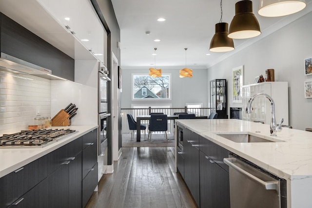 kitchen featuring stainless steel appliances, a spacious island, a sink, light countertops, and pendant lighting